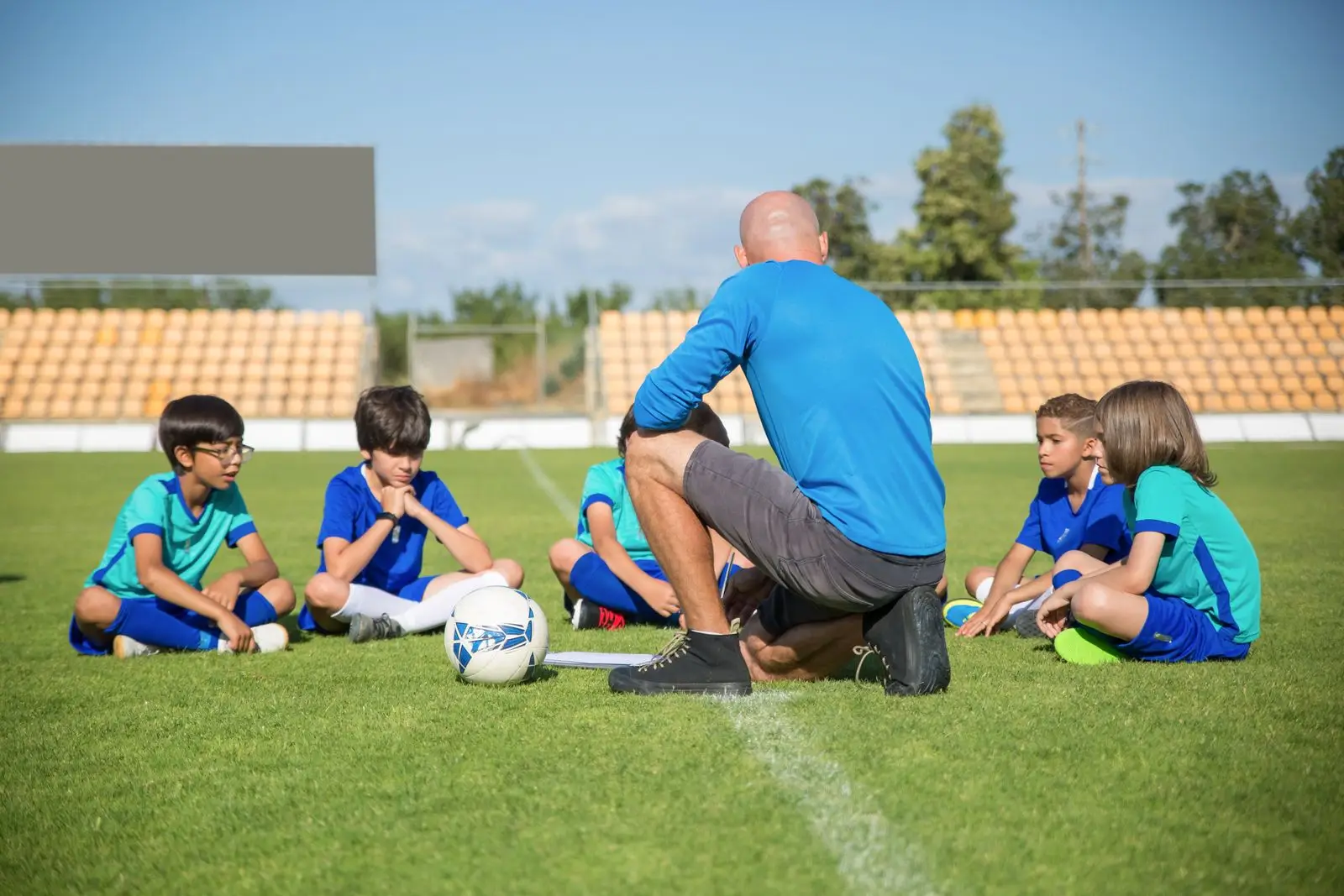 A coach kneeling at eye level, talking tactics with a group of attentive young players