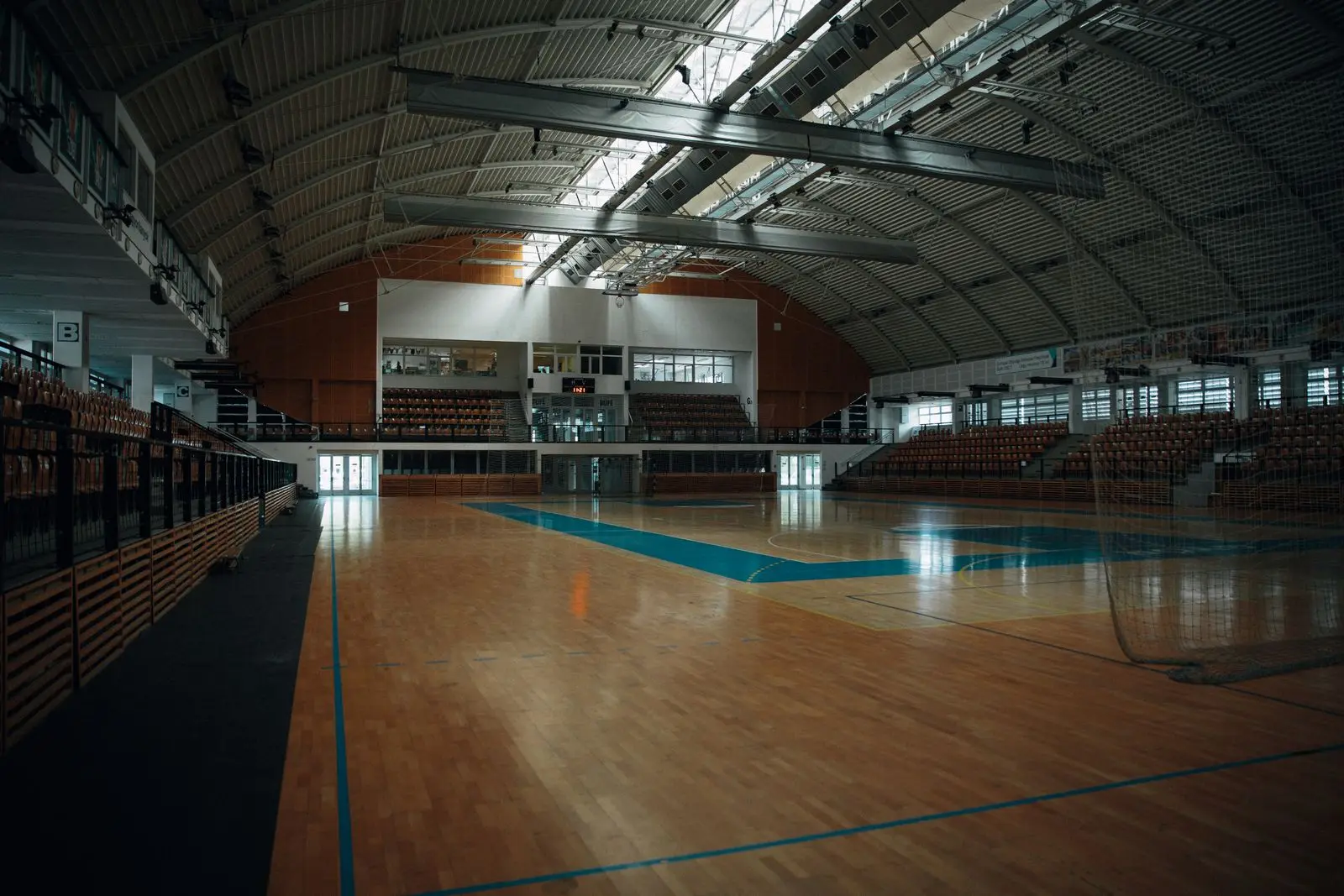 An empty indoor sports arena with polished parquet flooring, court markings and a goal
